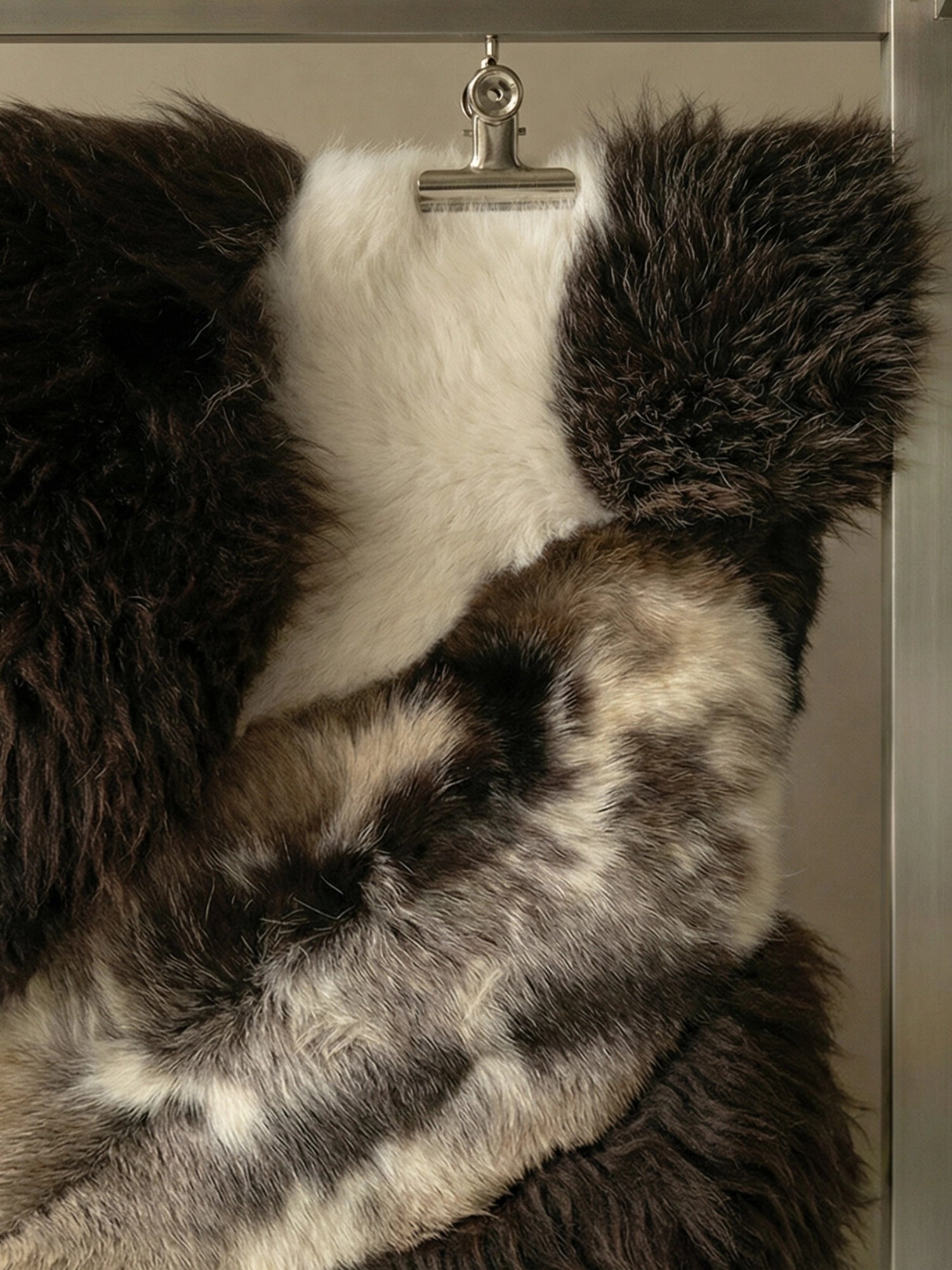 TCL Studios Brown Sheepskin Patchwork Rug, a luxurious natural sheepskin rug crafted from varying shades of plush, shaggy fur. This cozy floor covering features a rich blend of dark brown, creamy white, and mottled grey-brown patches, creating an organic, textured surface. Ideal as a statement accent rug for rustic living rooms, Scandinavian bedrooms, or cozy organic modern spaces.