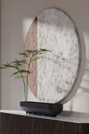 Decorative round mirror with a textured surface on a shelf with a plant.