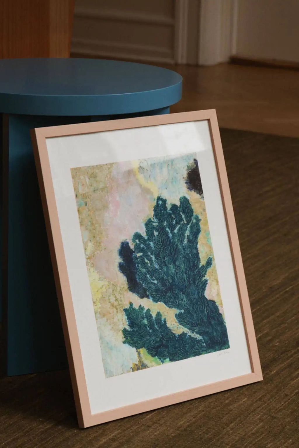 The Poster Club Vinca, an abstract botanical art print featuring a textured deep teal blue-green organic shape against a painterly background of muted pink, yellow, and earthy tones. This contemporary framed poster is housed in a delicate blush pink wood frame with a crisp white mat. Ideal for modern gallery wall art, bedroom decor, or stylish shelf styling in organic modern interiors.