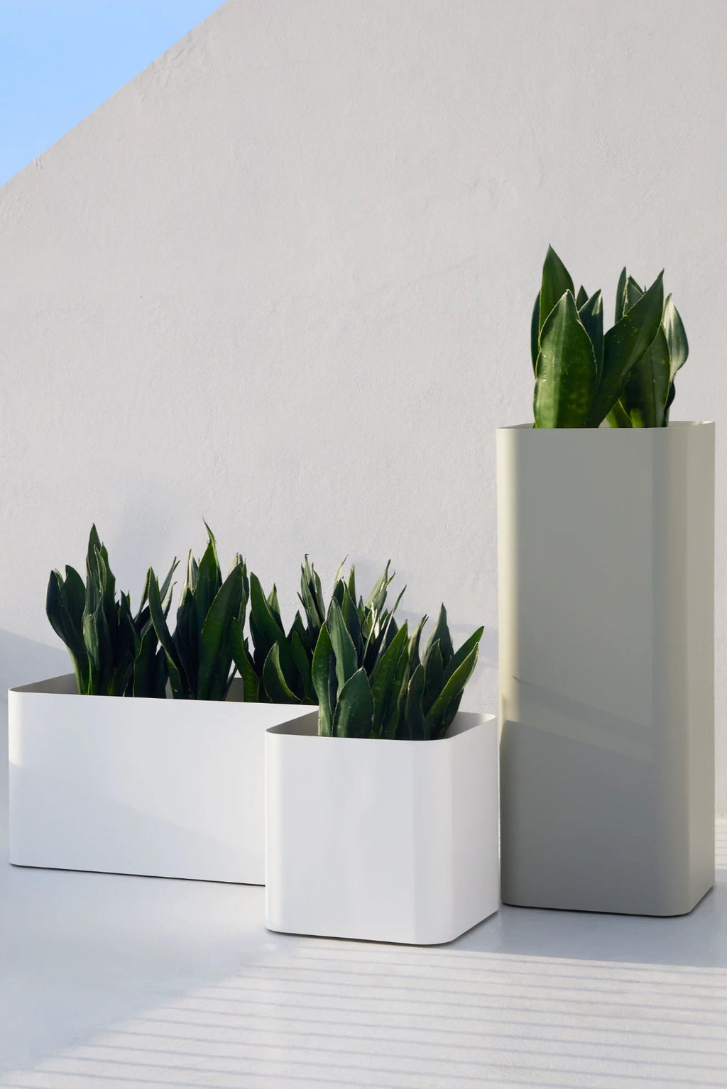 Gandia Blasco Sonora Outdoor Planter 1, a collection of sleek modern minimalist outdoor planters crafted from smooth, matte powder-coated metal. The set includes two white rectangular planters with soft rounded corners and one tall light grey columnar planter, designed for contemporary garden and patio spaces. These versatile outdoor plant pots are ideal for creating a clean, architectural look on a modern terrace, balcony, or entryway.