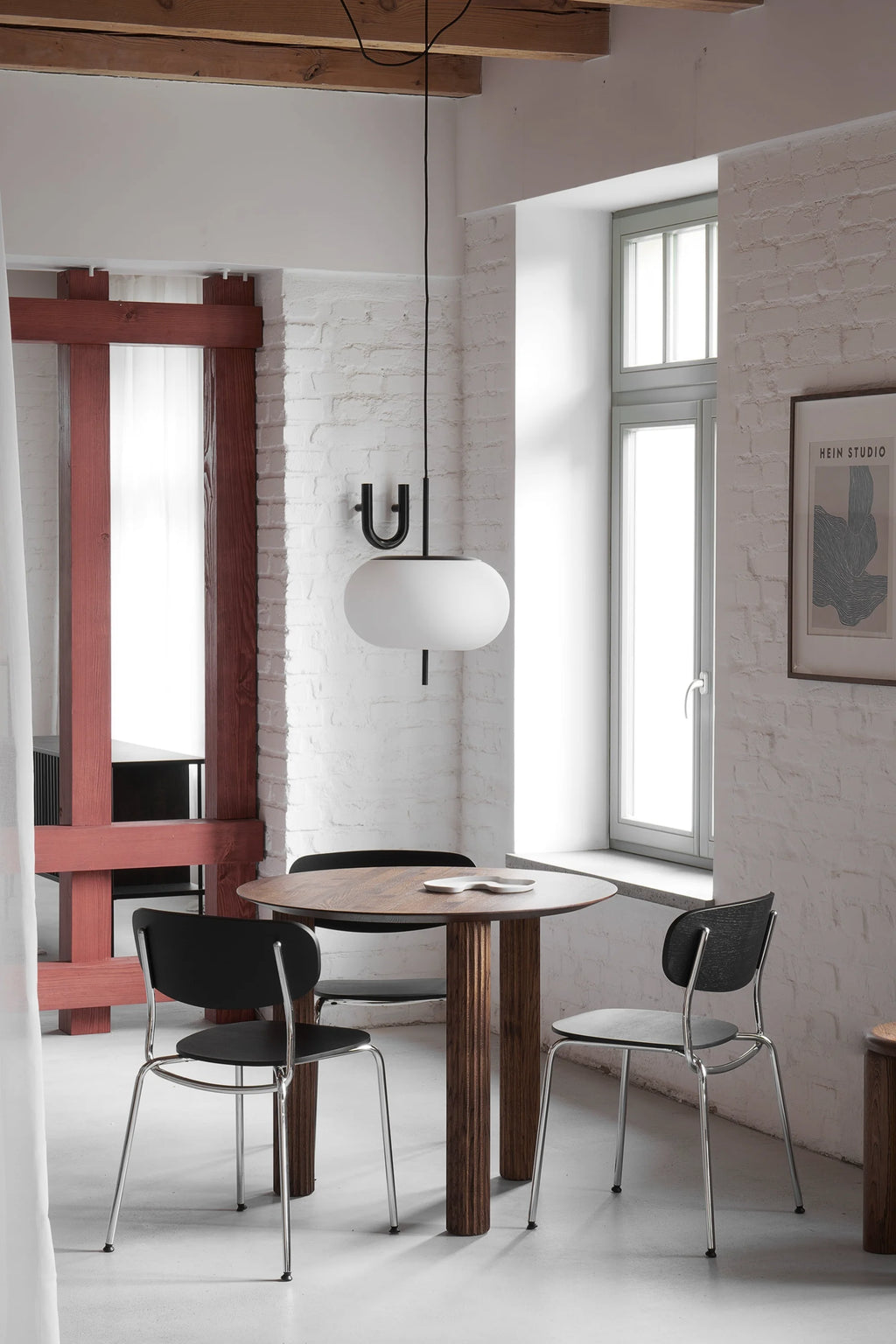 TAMO Filar Round Dining Table, showcasing a dark oak tabletop and three ridged, solid wooden legs, in a minimalist room setting with black chairs. Perfect for chic interior design.