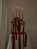 Decorative stoff nagel candle holder with red taper candles and red ribbons on a white tablecloth against a beige wall.