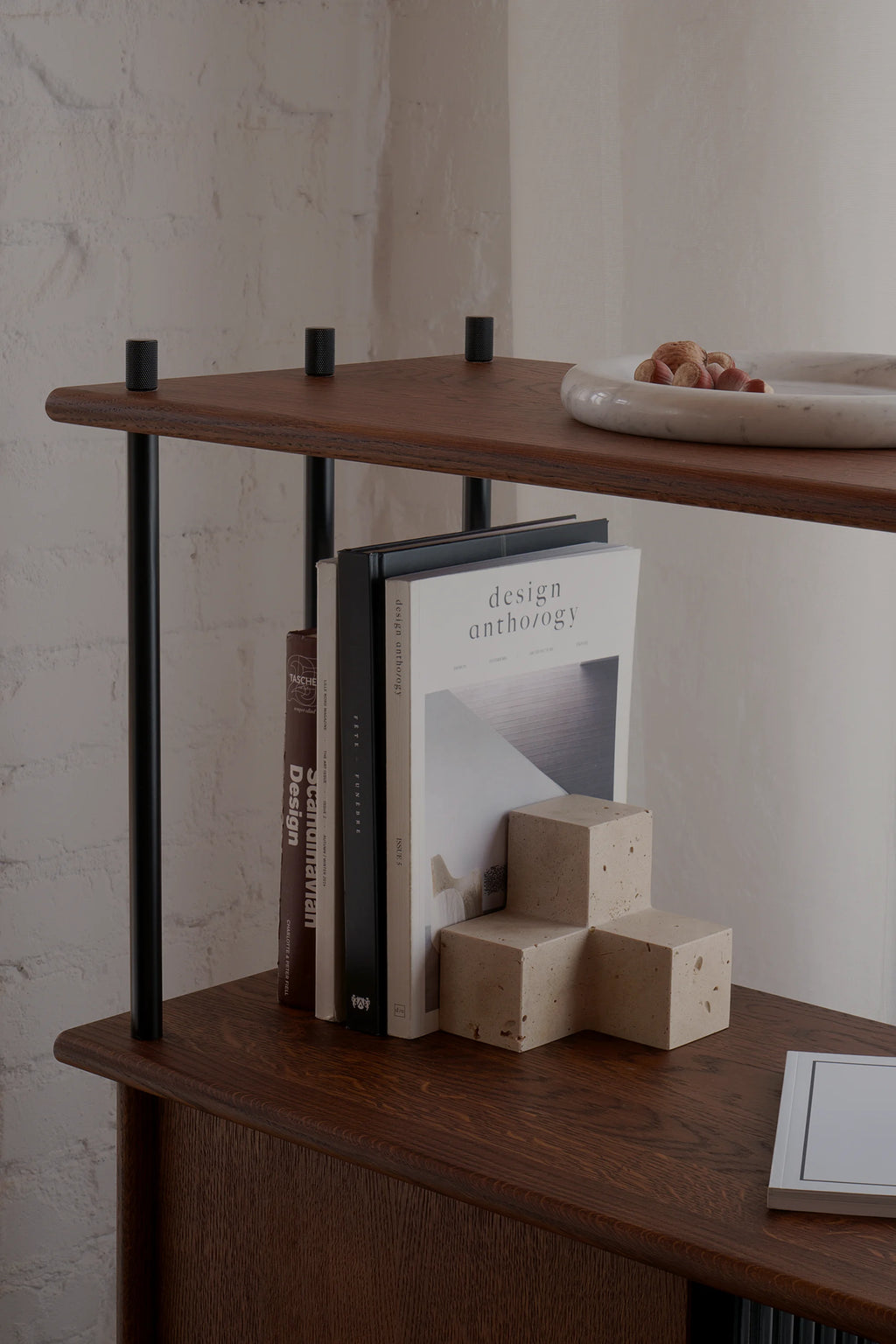 TAMO Tero Travertine Bookend in a lifestyle shot, displaying its unique geometric beige travertine with natural porous texture, elegantly holding books on a dark wood shelf. A premium decorative bookend for organizing sophisticated spaces.
