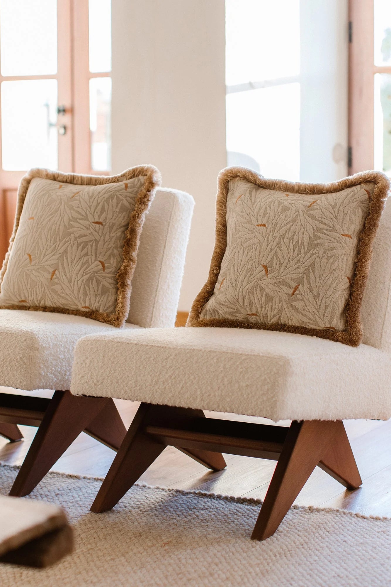Beige cushioned chairs with decorative pillows in a bright room.