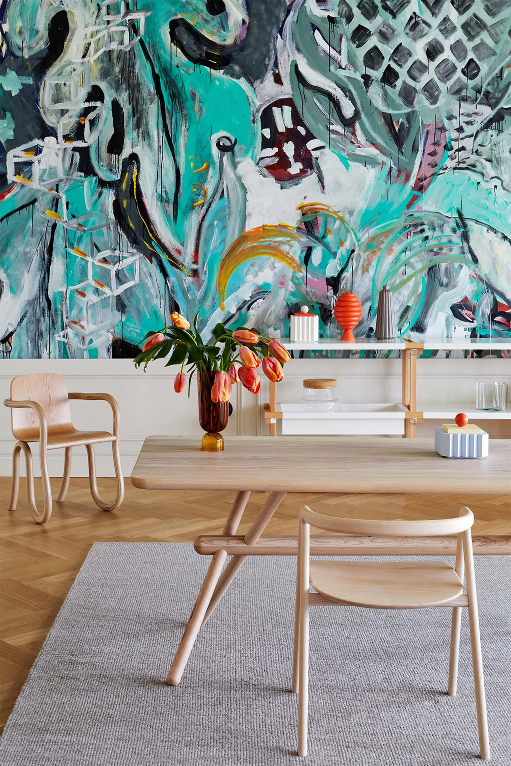 Made by Choice Laakso Dining Chair, a natural wood chair positioned next to a wooden dining table adorned with a vase of tulips, set against a striking abstract painting, illustrating a chic and artistic home interior.