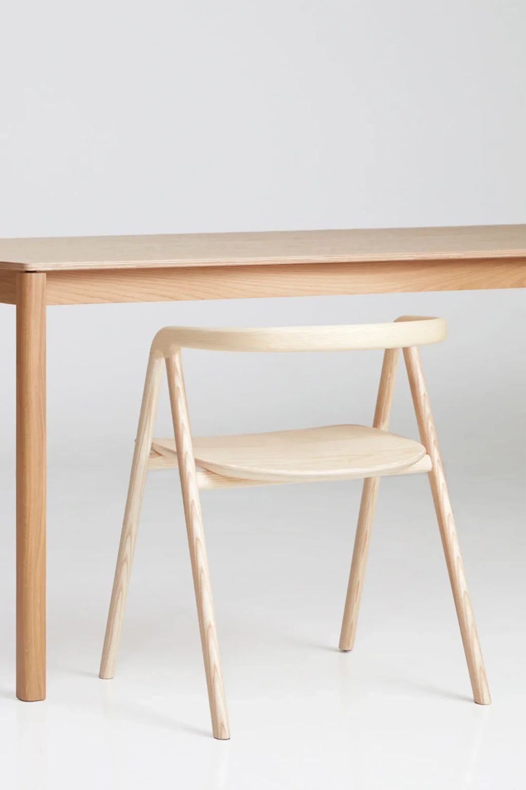 Made by Choice Laakso Dining Chair, a sleek and modern light wood chair with a gently curved backrest and seat, neatly tucked under a matching wooden dining table, presented on a clean white background.