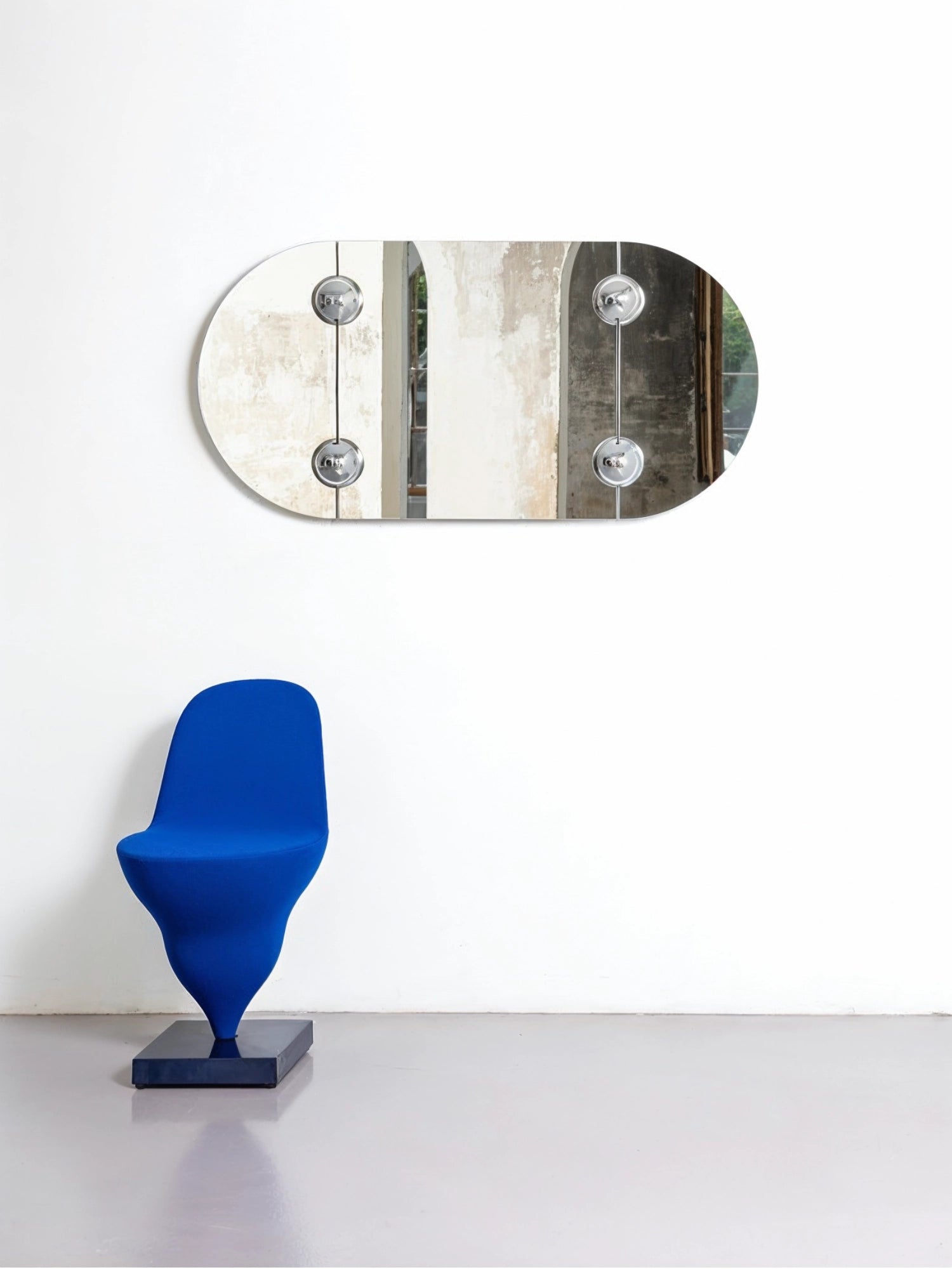 Moustache Sphera Oblong Mirror, a contemporary frameless glass mirror with rounded edges and four chrome spherical fasteners, reflecting an interior space with a blue sculptural chair.