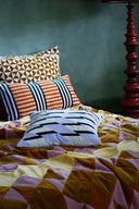 Colorful bedding with patterned pillows on a bed against a green wall.