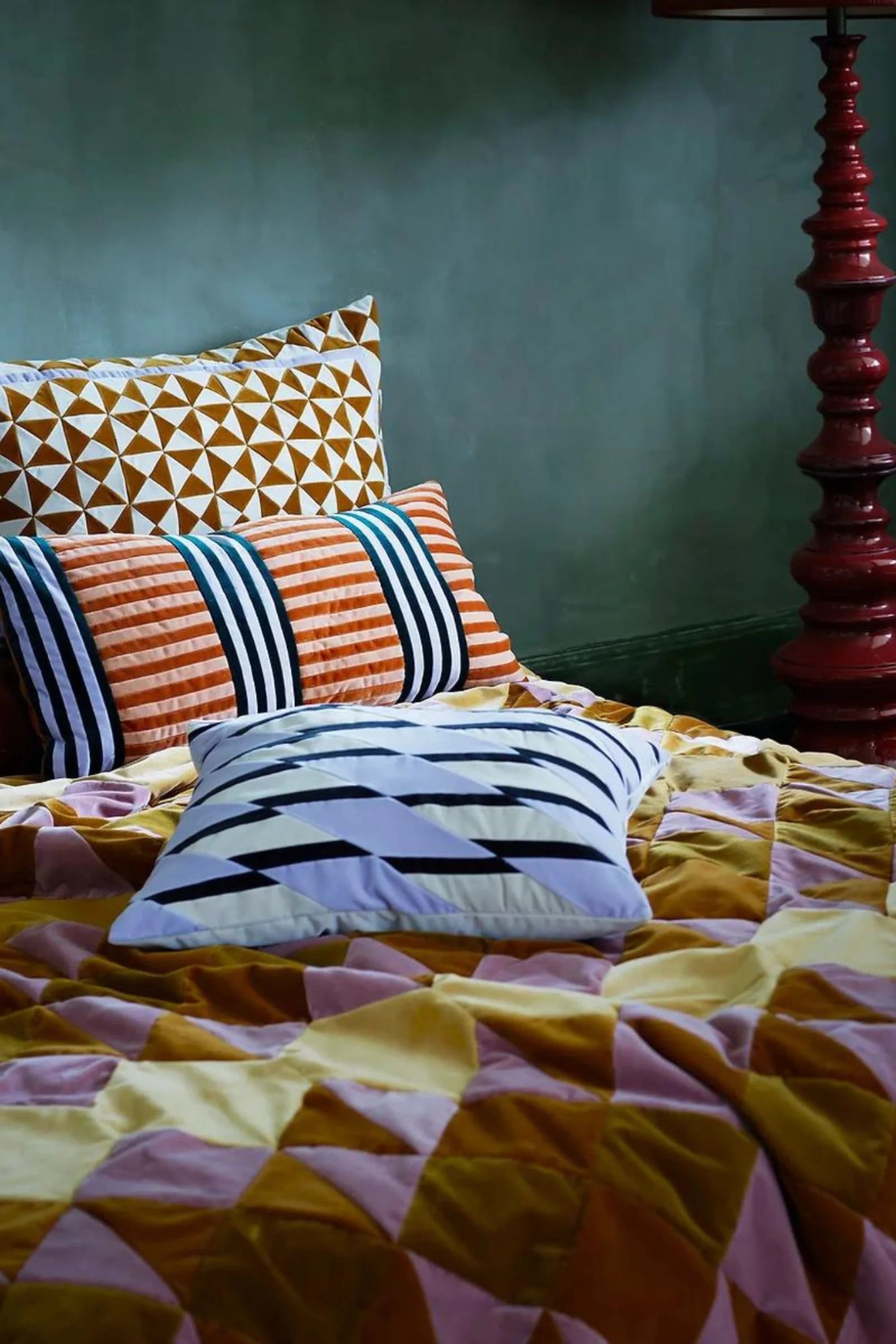 Colorful bedding with patterned pillows on a bed against a green wall.
