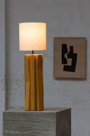 Yellow table lamp on a gray pedestal with abstract wall art in the background