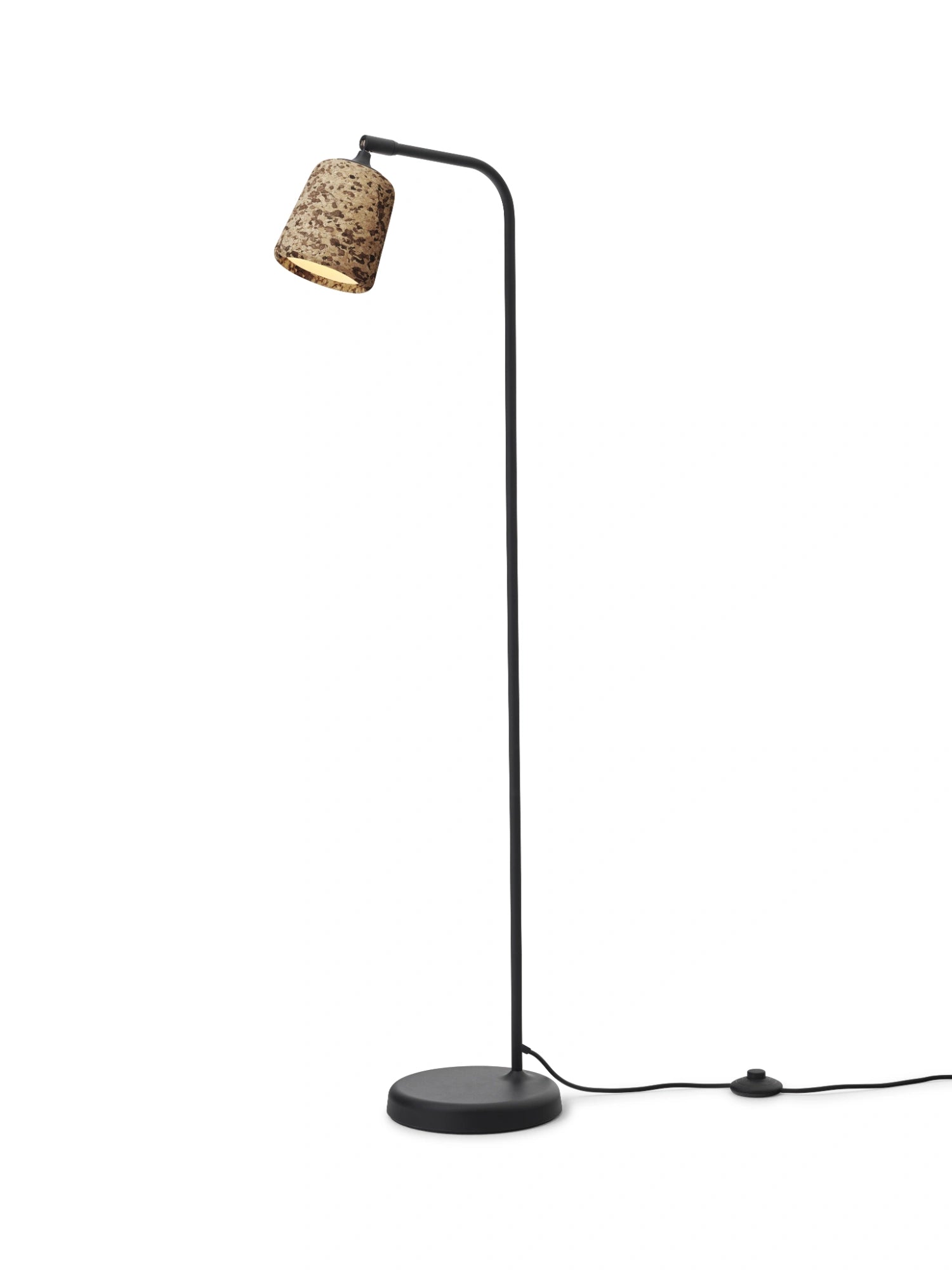 New Works Material Floor Lamp, a modern minimalist floor lamp featuring a sleek matte black metal frame with a slender stem, curved arm, and round base, topped with a distinctive cylindrical natural cork lampshade showcasing a mottled, textured pattern. Ideal as a Scandinavian reading lamp for living rooms, bedrooms, or contemporary home offices.