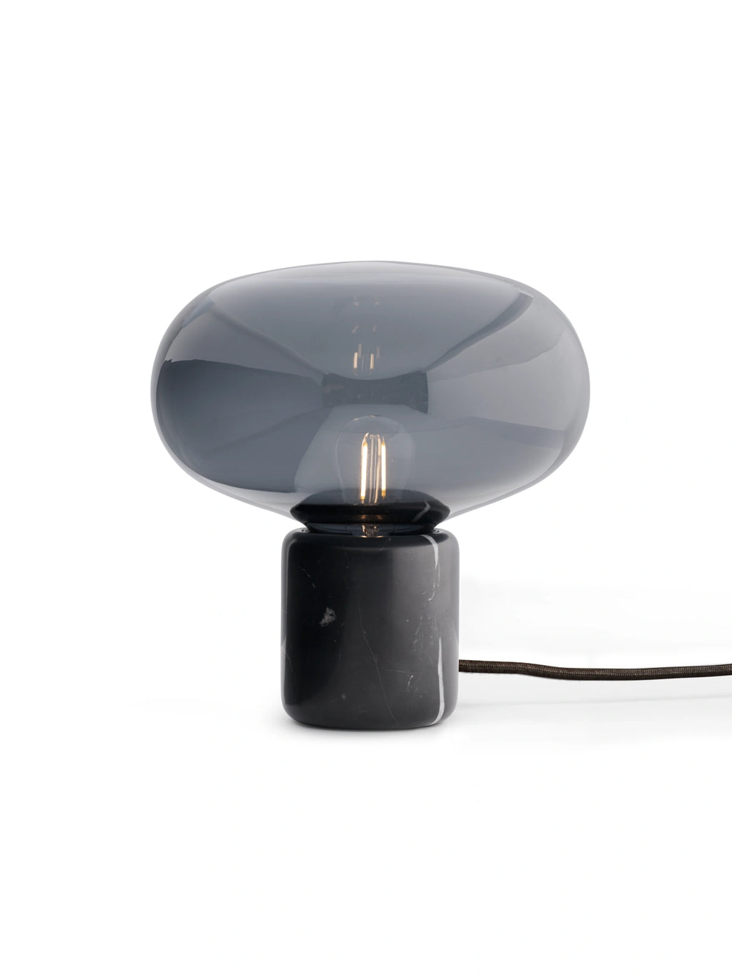 New Works Karl-Johan Table Lamp, a luxury mushroom-shaped lamp with a smoked grey glass shade and black marble base, featuring a visible filament bulb. Perfect for modern interior styling.