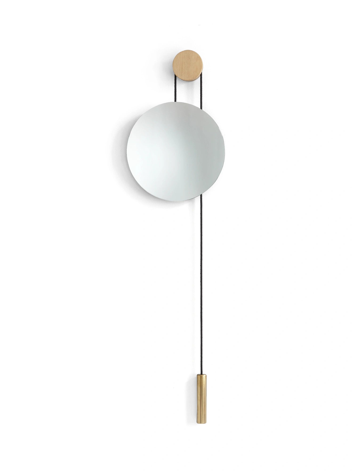 New Works Rise & Shine Wall Mirror, a modern round silver mirror suspended by a black cord, natural oak wood pulley, and a luxurious brass weight, against a white wall. Ideal for minimalist interiors.