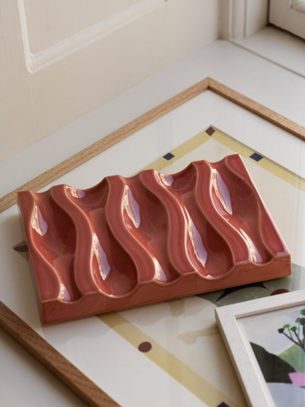 The Poster Club Echo Relief No. 02, a contemporary sculptural wall art piece crafted from glazed ceramic in a warm, glossy terracotta hue with five undulating, organic wave-like ridges.