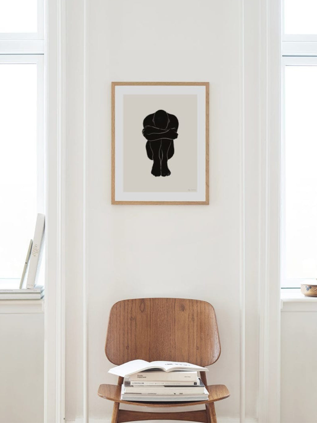 The Poster Club STATIC 02, a modern minimalist abstract art print featuring a bold black silhouette of a curled-up figure against a soft light beige background, framed in natural oak with a crisp white mat. This Scandinavian-style framed poster is perfect for contemporary gallery walls, bedroom decor, or a serene living room accent.