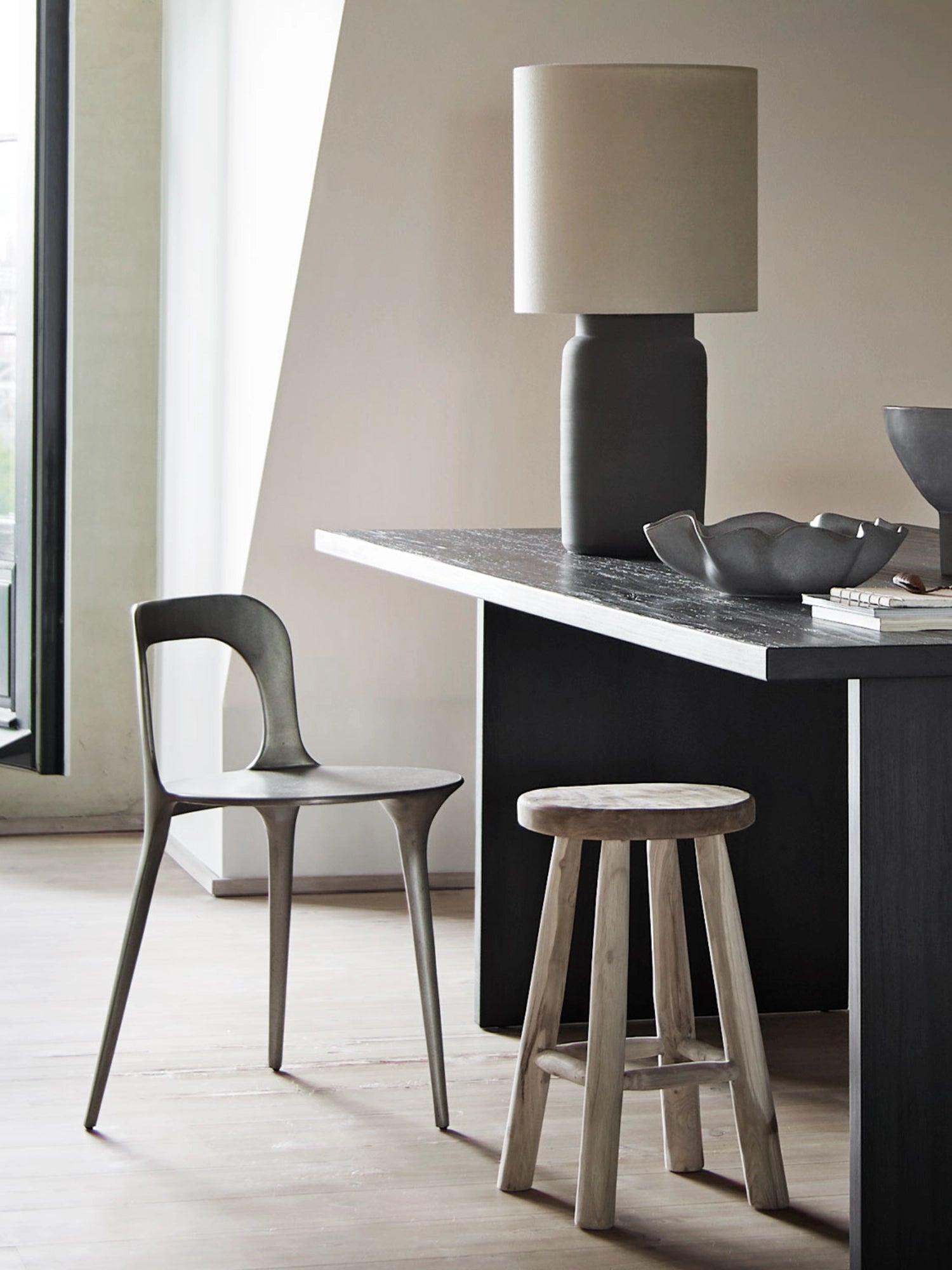 Tine K Dune Recycled Aluminium Chair, a dark grey matte finish chair crafted from sustainable recycled aluminium, featuring a distinctive organic, sculptural form. Its fluid design includes a gracefully curved backrest with a unique cutout and subtly flared legs, embodying a sleek contemporary aesthetic. Ideal as a minimalist dining chair or a modern accent chair for design-conscious interiors.