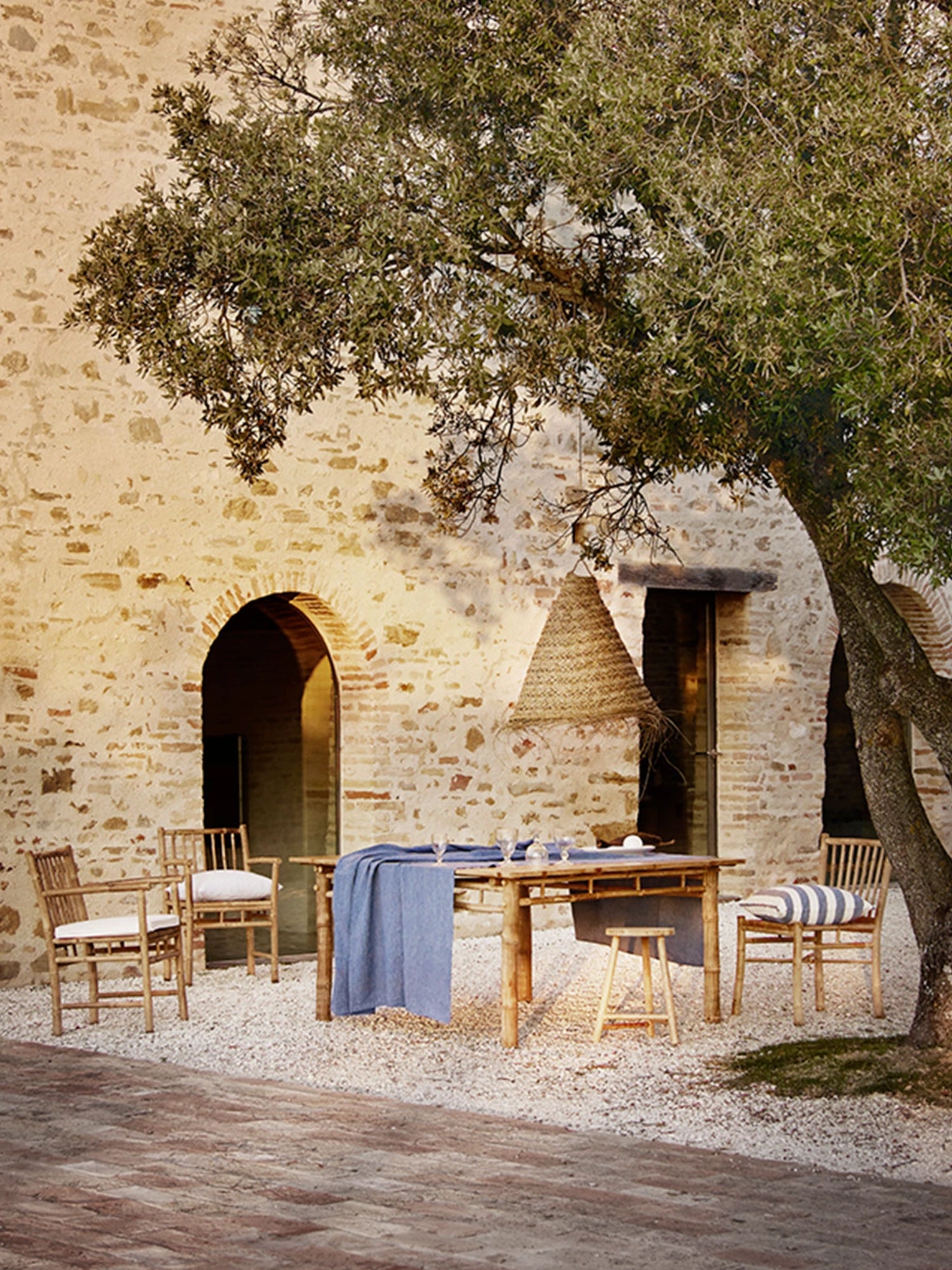 Tine K Outdoor Bamboo Dining Chair With Armrest - Set of 4, featuring a warm natural bamboo construction with a light brown finish, slatted backrest, and sturdy armrests, designed for comfortable al fresco dining. These rustic outdoor dining chairs include soft white linen cushions, perfect for creating an inviting Mediterranean or organic modern patio living space or garden setting.