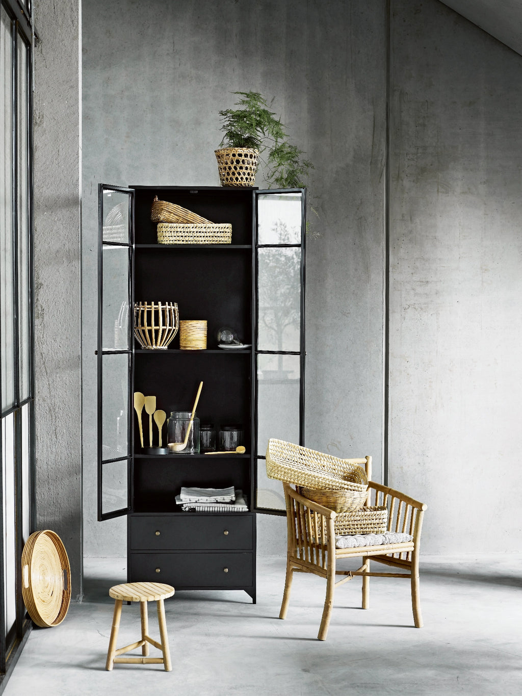 Tine K Metal High Cabinet, a tall industrial chic display cabinet crafted from matte black metal with clear glass paneled doors and two lower solid drawers featuring brass knob handles. Its clean lines and minimalist design offer versatile storage and display, blending modern aesthetics with functional organization. Perfect as a contemporary living room cabinet, kitchen pantry, or dining room display unit for industrial or modern interiors.