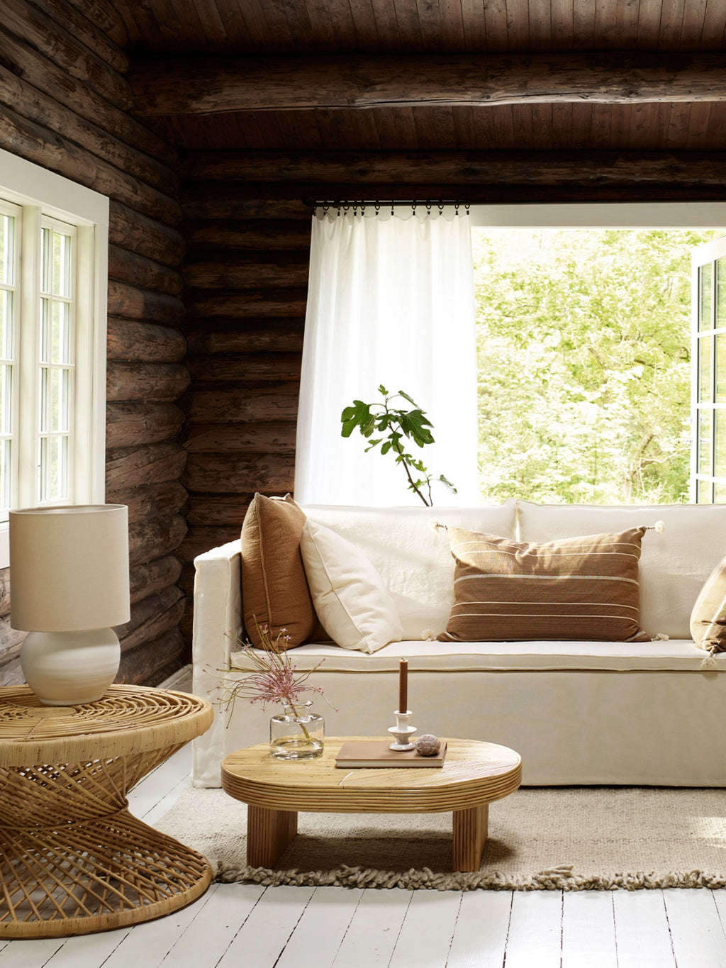 Tine K Viva Rattan Table, an organic modern oval coffee table crafted from natural woven rattan with a slatted or reeded cylindrical base, featuring a light, warm blonde finish. This contemporary rattan and wood coffee table offers a soft, textured accent for Scandinavian, coastal, or boho living rooms.