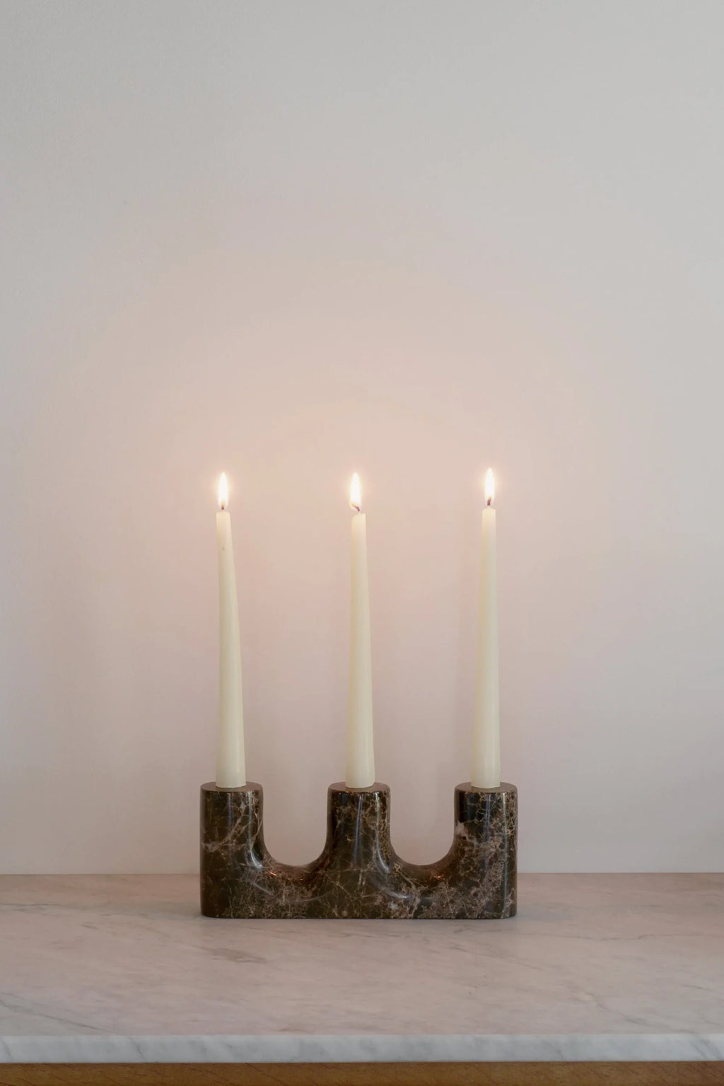 TAMO Trilo Candle Holder, a premium dark brown marble candelabra with three lit white taper candles, displayed on a light marble surface. Perfect for elegant home decor.
