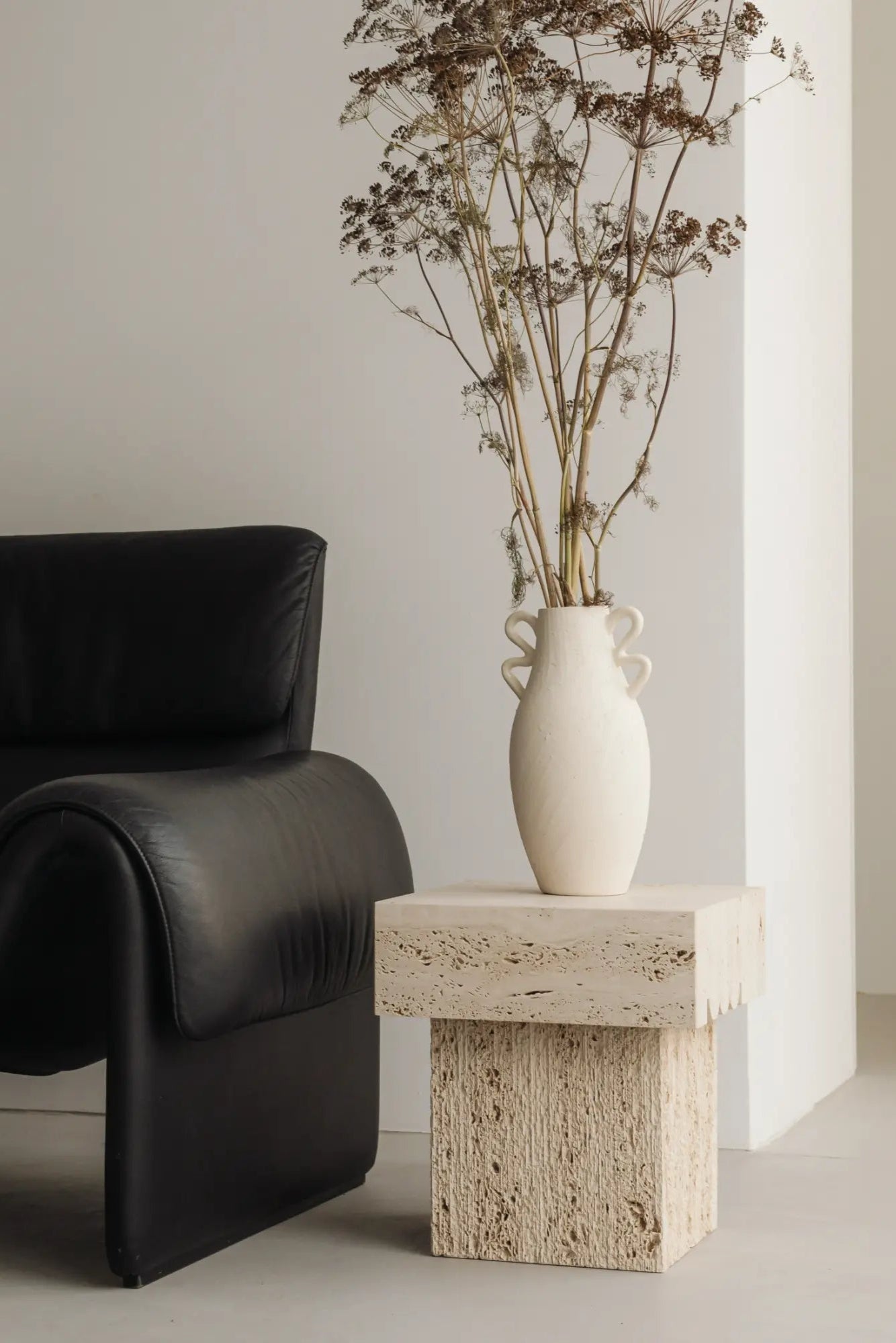 un'common Oro Side Table, a sculptural beige travertine side table crafted from two stacked rectangular blocks of natural porous stone. It features a rough, textured finish with visible natural stone pores, offering a distinctive brutalist and organic modern aesthetic. Perfect as a minimalist accent table for contemporary living rooms or a unique bedside table.