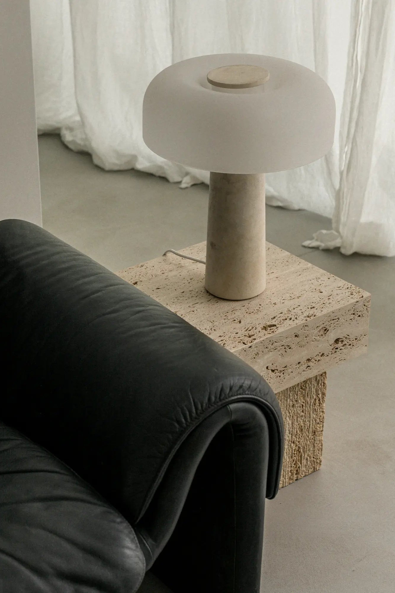 un'common Oro Side Table, a minimalist side table crafted from natural porous travertine stone in warm beige tones, featuring a solid rectangular block top and a sturdy block base with visible raw textures. This brutalist-inspired travertine end table is perfect for organic modern living rooms or contemporary bedroom accents.
