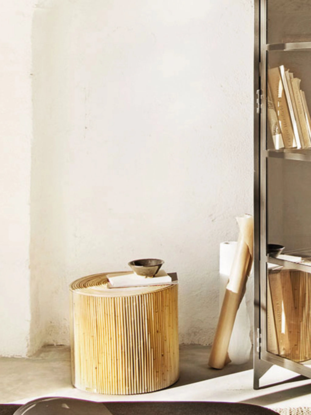 Tine K Viva Rattan Stool, a cylindrical natural blonde rattan side table featuring a distinctive ribbed texture from vertically arranged rattan poles. This organic modern and bohemian accent piece offers natural warmth and a relaxed aesthetic. Ideal as a versatile end table, bedside stool, or decorative element for living rooms, bedrooms, or coastal-inspired spaces.