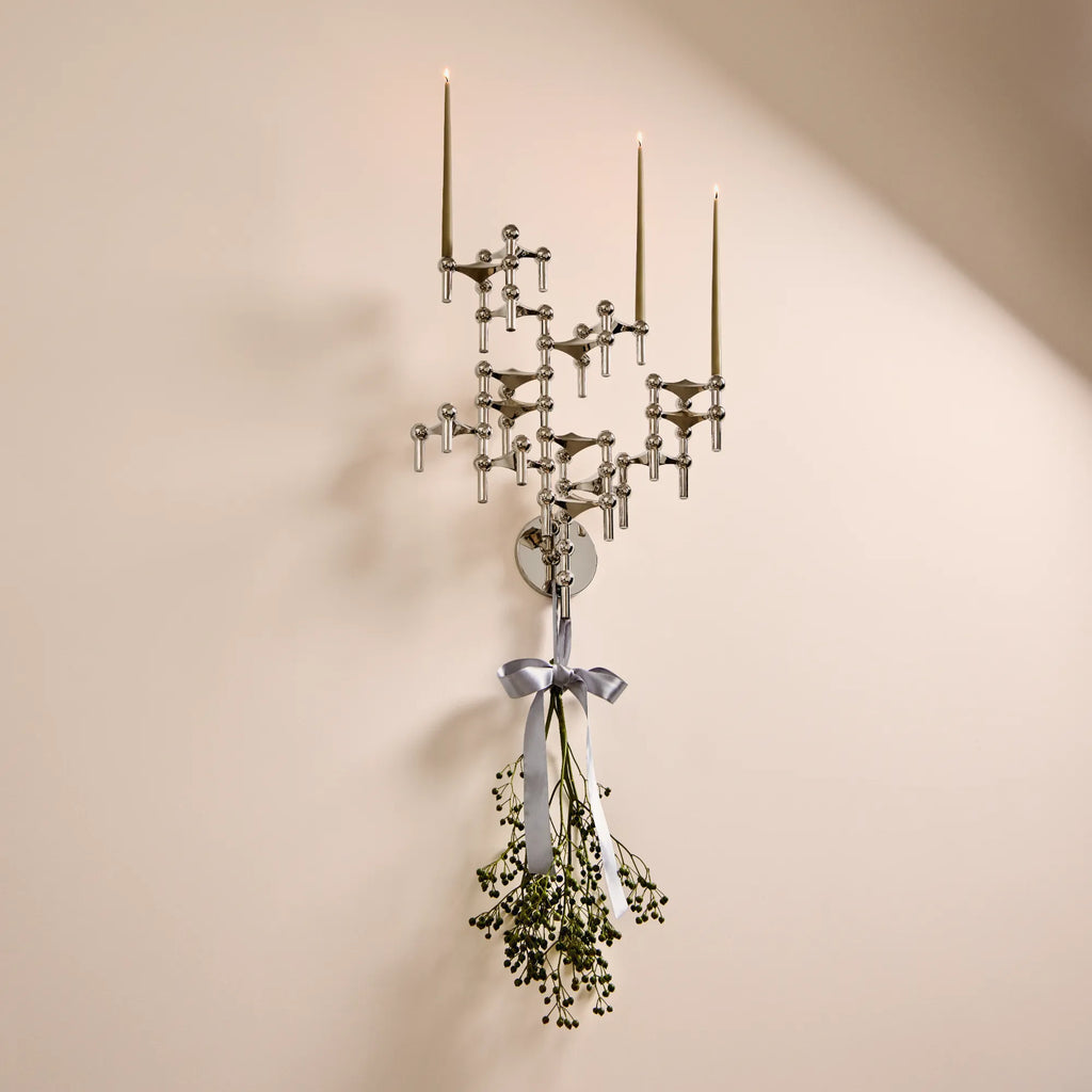 Stoff Nagel Wall Hanger Candle Holder - Chrome - Configuration 3, a striking mid-century modern modular candle holder crafted from polished chrome-plated metal, featuring an intricate, interconnected geometric design. This sculptural wall sconce holds multiple olive green taper candles, creating a captivating display.