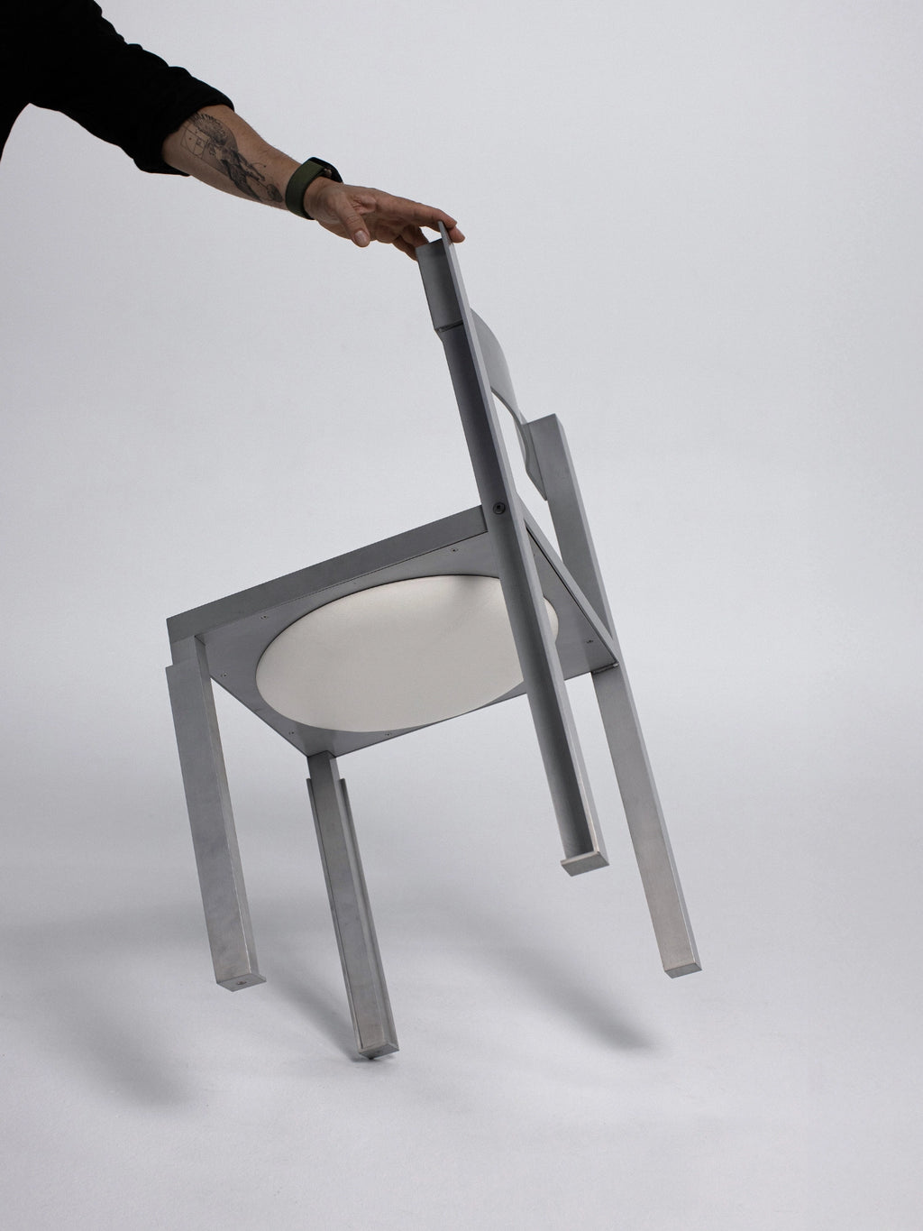 YET. Strut Chair, a striking contemporary industrial dining chair featuring a geometric brushed aluminum frame in a matte silver finish with bold, angular lines and exposed structural elements. Its minimalist brutalist design includes a contrasting round white upholstered seat. Ideal as a modern dining chair for industrial chic interiors or minimalist kitchen dining areas.