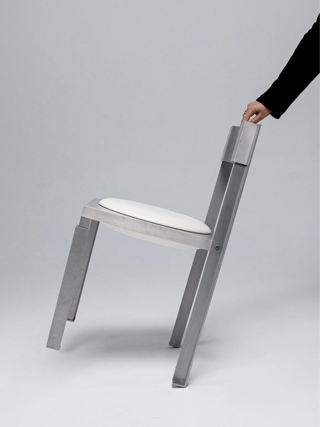 YET. Strut Chair, a striking industrial chic dining chair featuring a brushed silver aluminum frame with a raw, geometric construction and angular legs. Its minimalist design includes a contrasting crisp white upholstered oval seat, emphasizing its contemporary brutalist aesthetic. This modern metal chair is perfect for a minimalist dining room, industrial kitchen, or as a statement piece in a contemporary office.