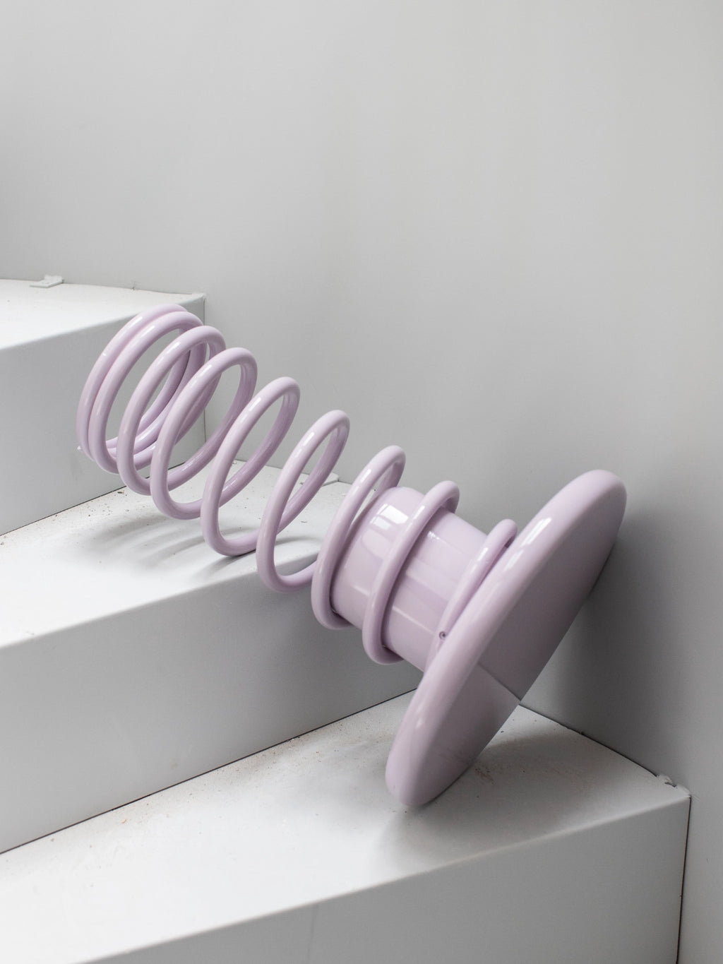 YET. Twist Stool, a modern sculptural stool in a pastel lilac finish, featuring a unique coiled spiral body that resembles a spring and a sturdy flat base. Crafted from glossy lacquered metal, this playful design offers a smooth, reflective surface. Ideal as an accent stool or side table for contemporary living rooms, vibrant bedrooms, or postmodern interior styling.